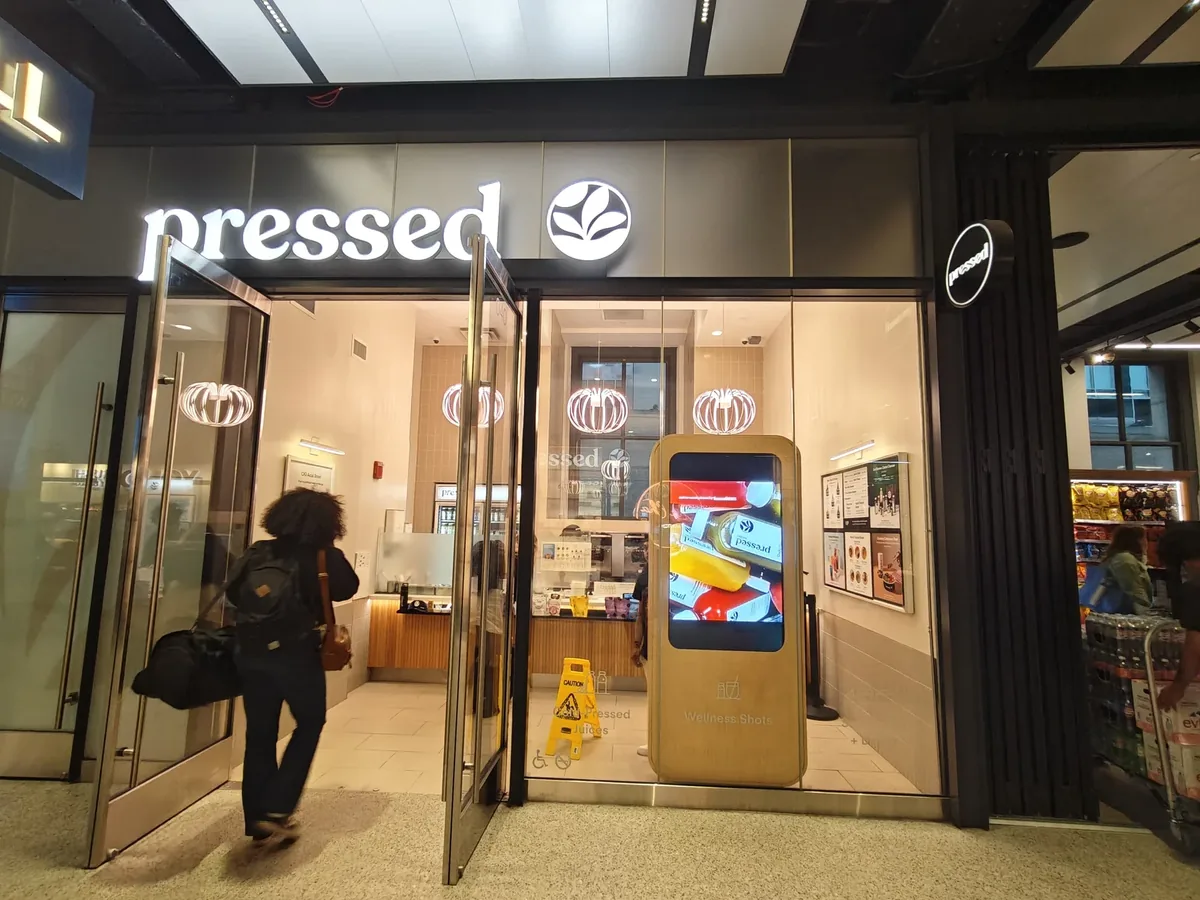 Pressed Juicery storefront at Moynihan Train Hall with a birch digital kiosk inside the entrance